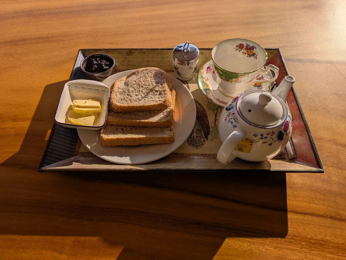 Bread, butter and preserve with a tea service on a sunlit wooden table.